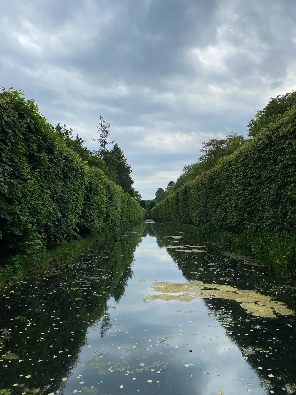 A straight canal bordered by tall manicured hedges in a formal garden.