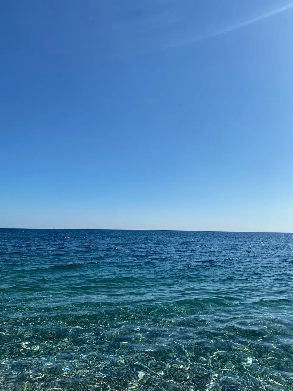 Crystal-clear turquoise shallows over a rocky seabed beneath a cloudless blue sky.
