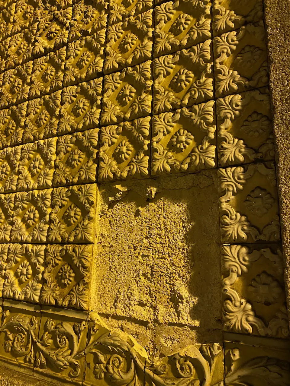 Ornate yellow ceramic tiles with a missing section revealing rough stone underneath.