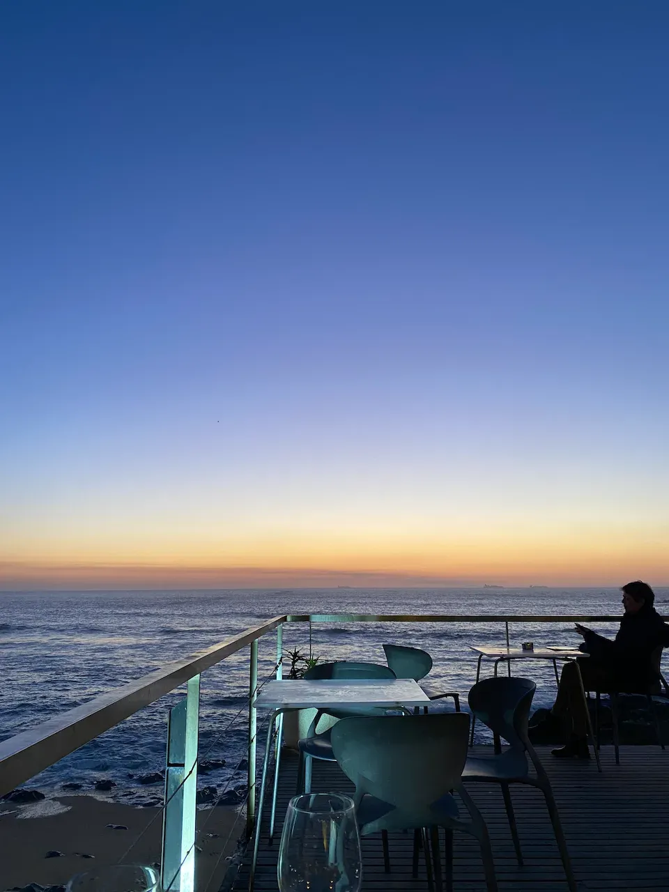 Seaside restaurant terrace at sunset with modern chairs overlooking the ocean.