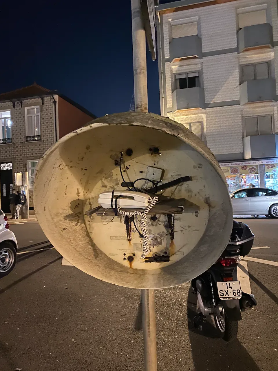 A weathered public telephone hood with a corded landline phone on a city street at night.