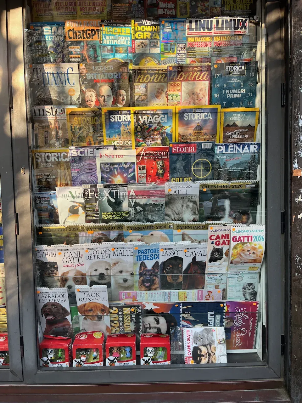 Italian newsstand display with magazines on AI and history, and 2026 animal calendars.