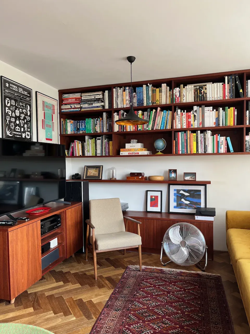 Mid-century modern living room with wooden bookshelves, TV console, and patterned rug.