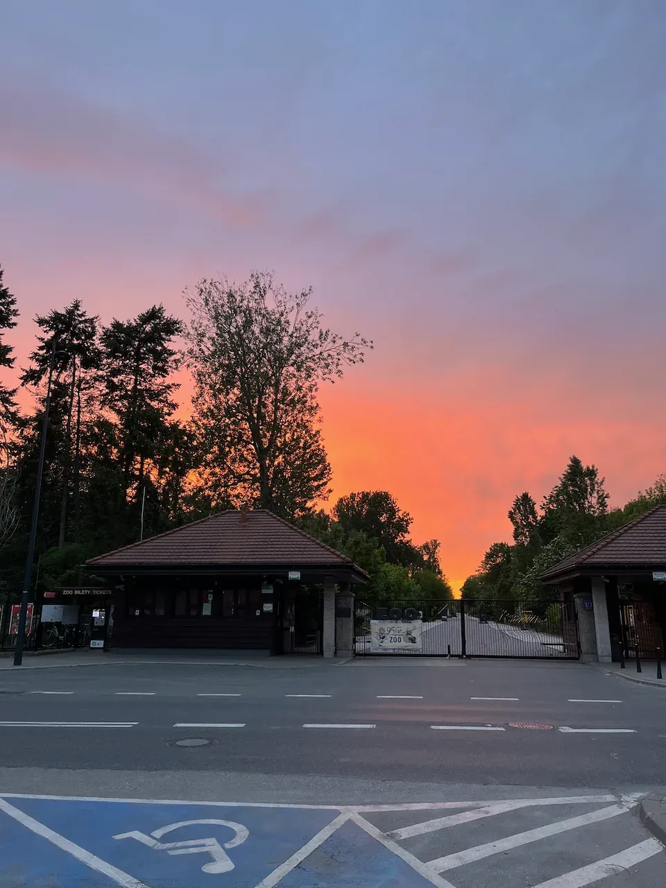 Zoo entrance at sunset with ticket booths silhouetted against an orange and pink sky.