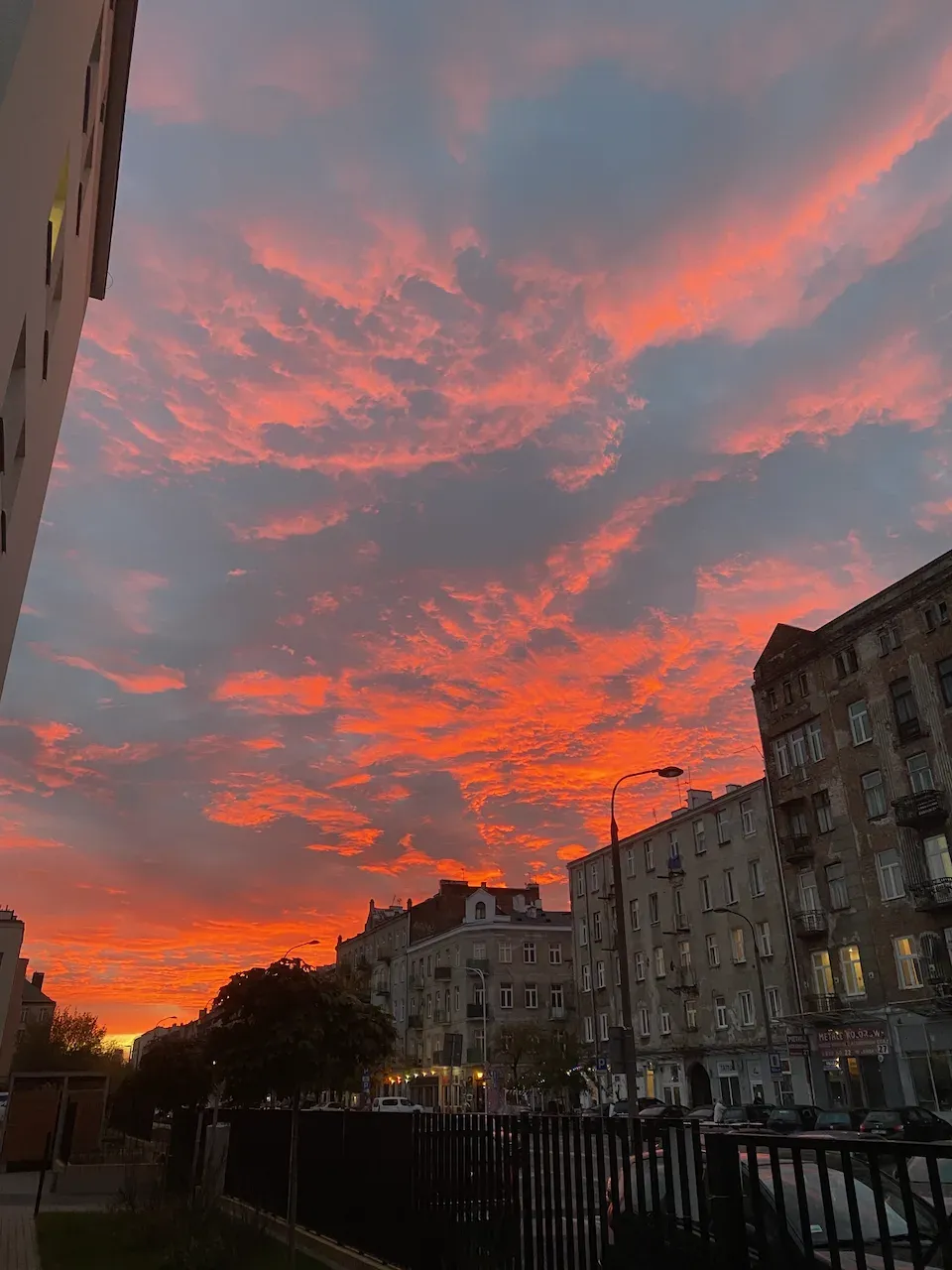 Fiery orange and pink sunset clouds over a city street with apartment buildings.