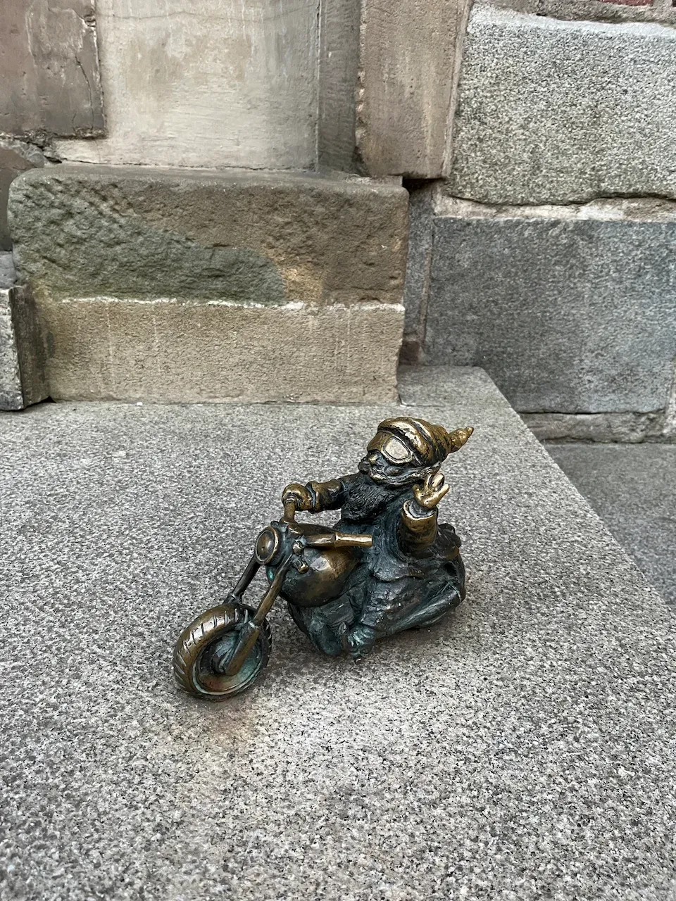 Bronze dwarf gnome sculpture riding a motorcycle and making a peace sign.