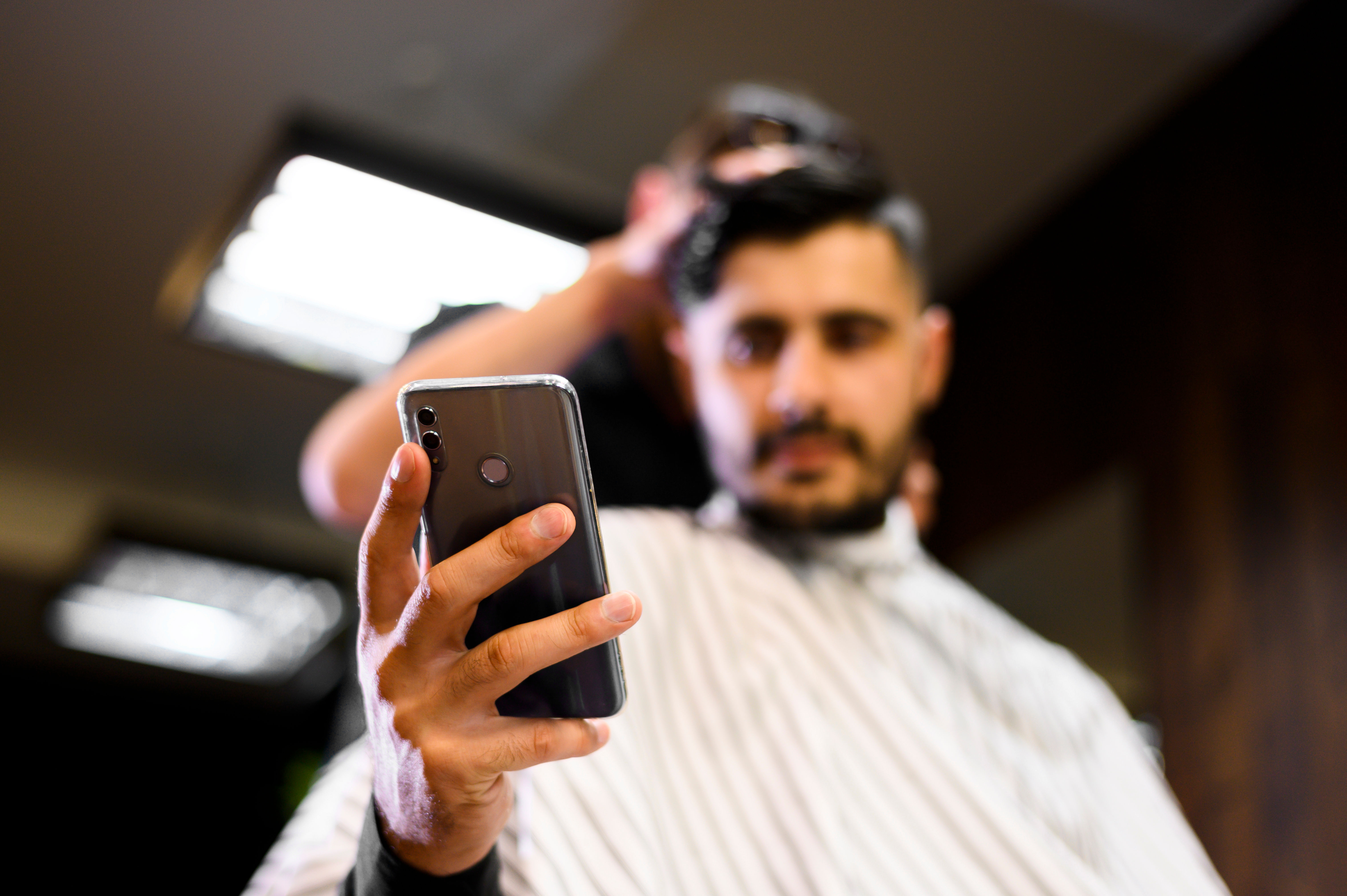 Homme qui profite d’une prestation de coiffeur à domicile, naviguant sur son téléphone