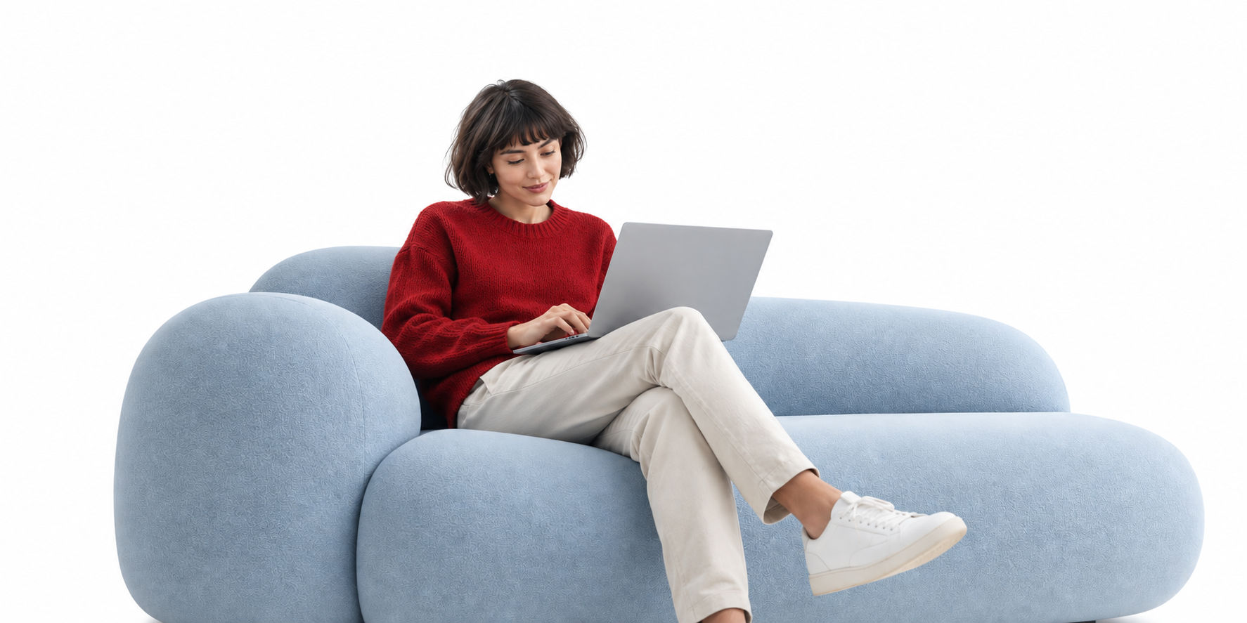 A woman in a red sweater working on a laptop while seated on a pale blue sofa