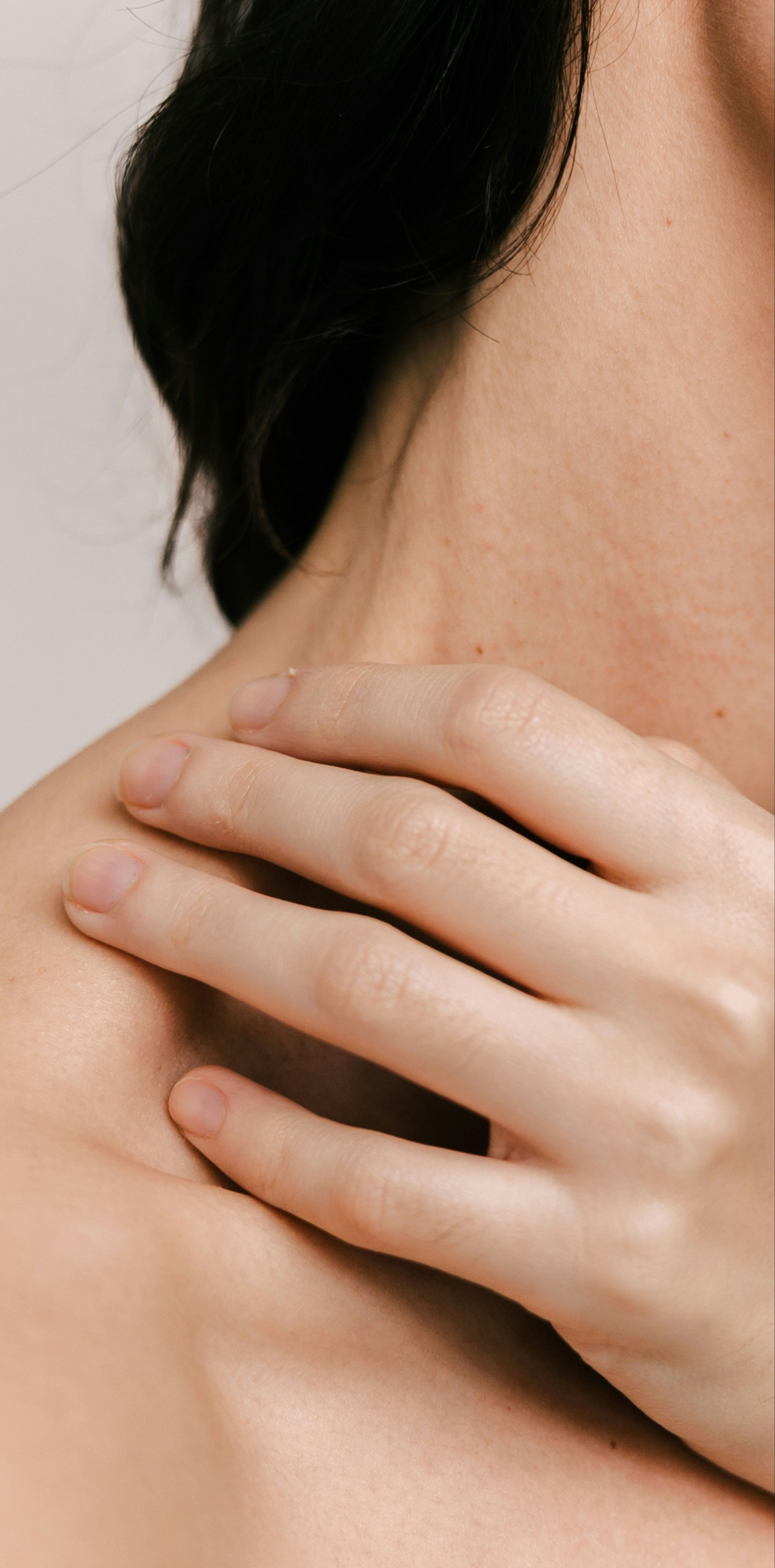 A close-up of a person's neck and shoulder with their hand resting lightly on the collarbone.