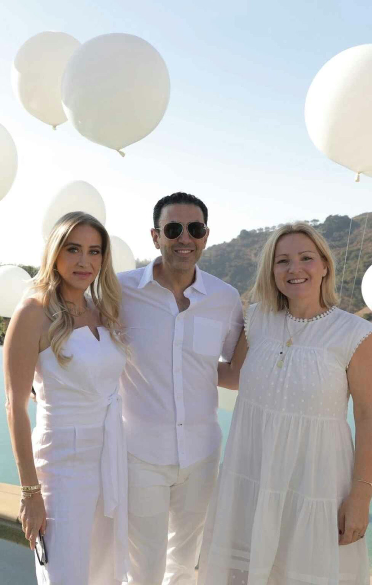 Three Beyond Beauty Club members dressed in white outdoors, with balloons behind them