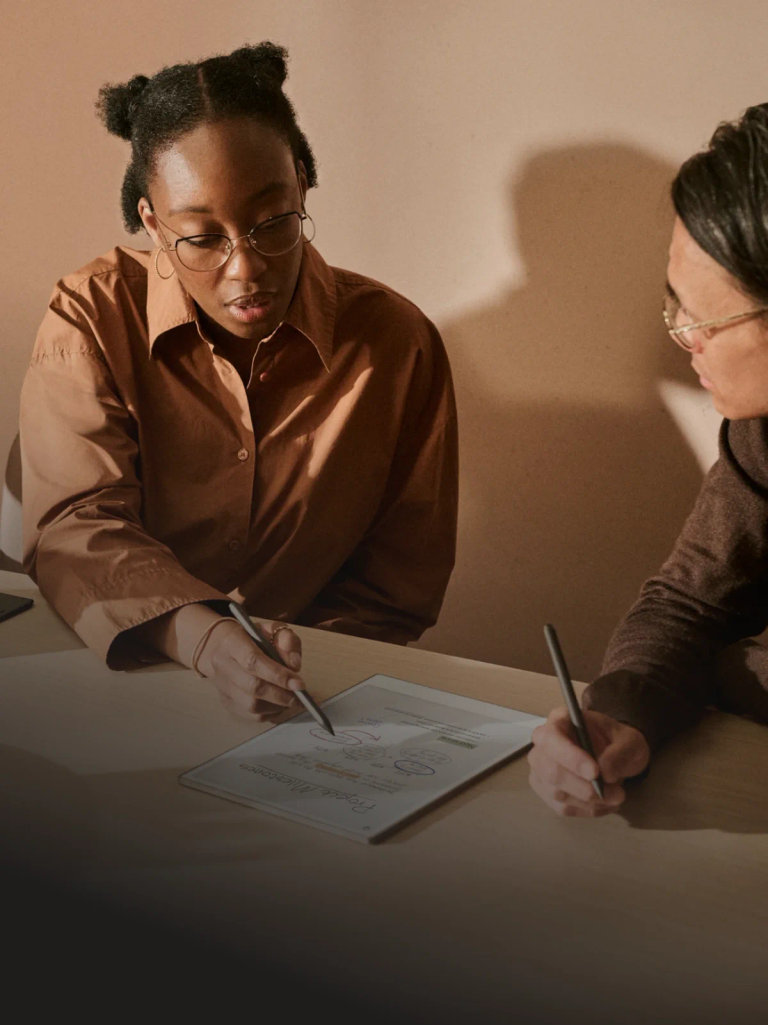 Two people reviewing notes on a reMarkable paper tablet, writing with the Marker.