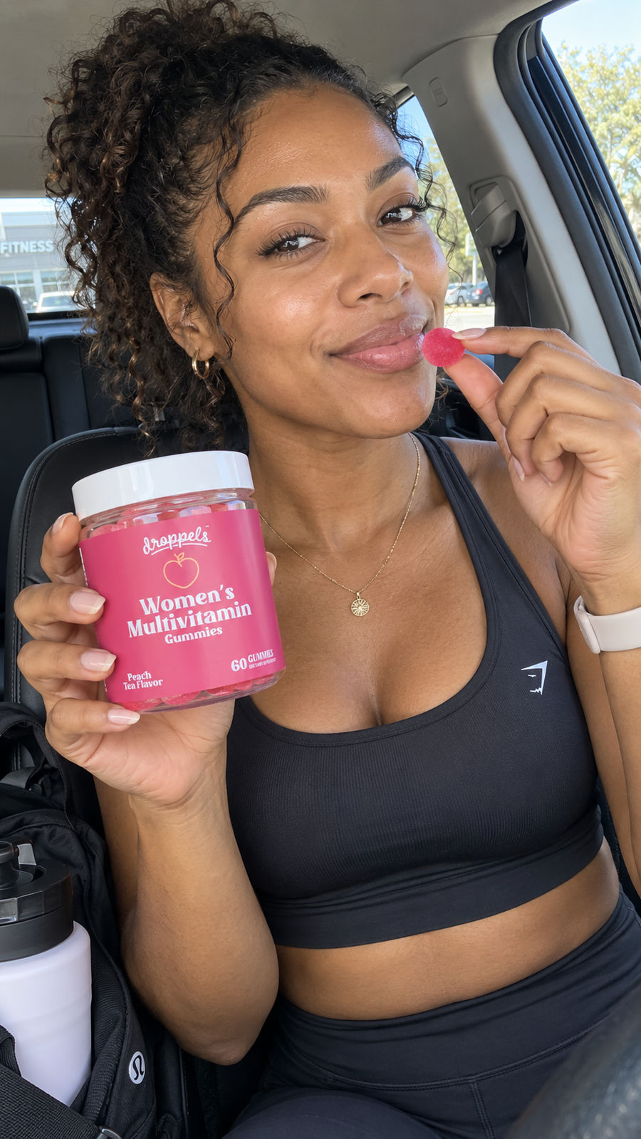 Woman holding a pink gummy and a bottle of Droppels Women’s Multivitamin Gummies