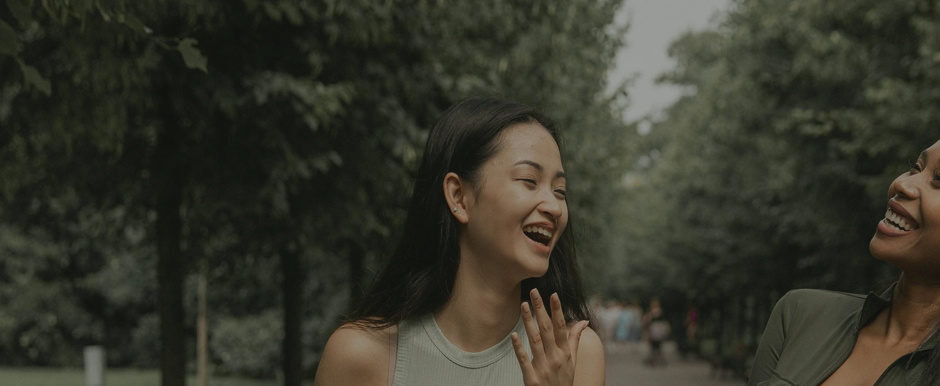 Two women laughing joyfully together in an outdoor setting with trees in the background