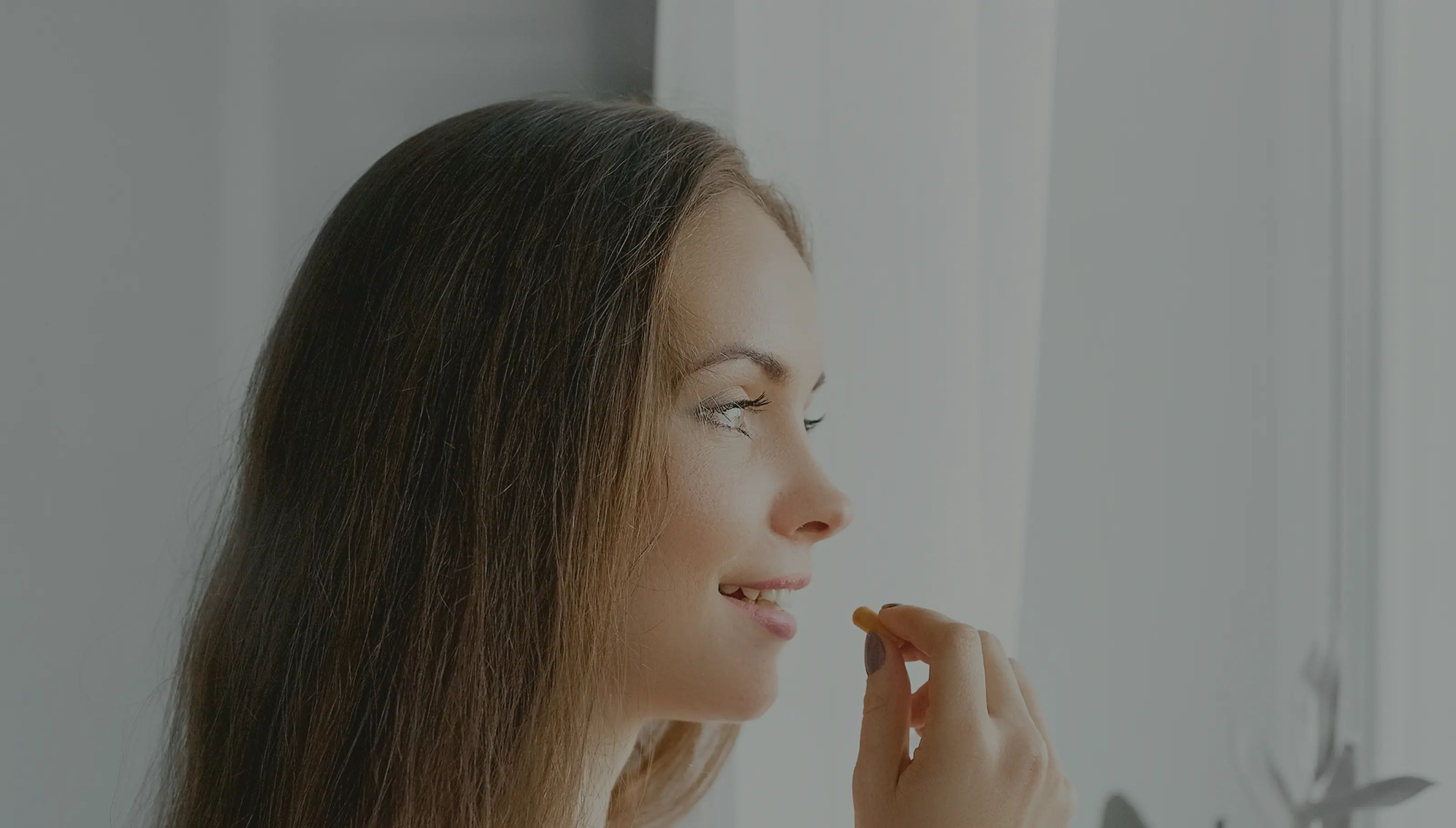 A woman holding a pill close to her mouth.