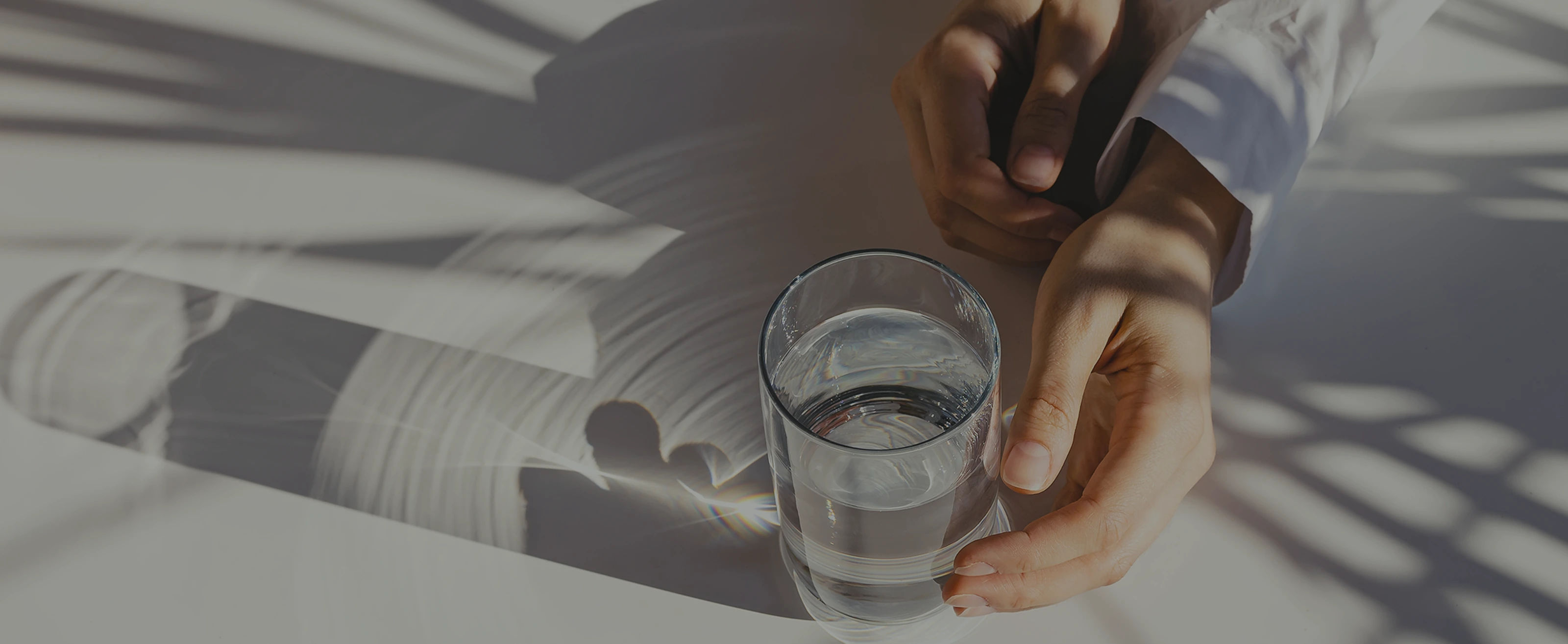 Hands holding glass of water with shadow patterns