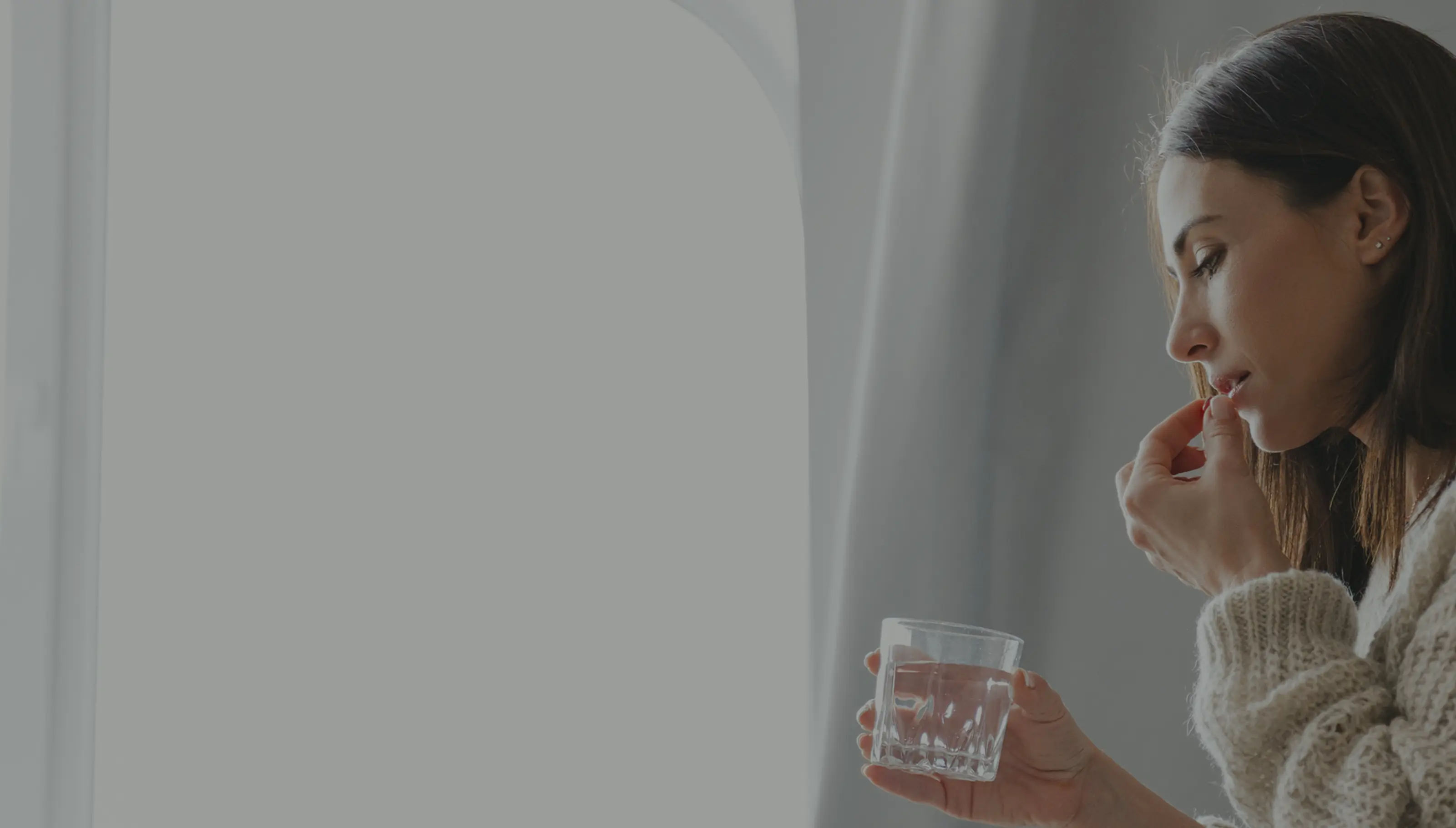 A woman placing a pill in her mouth and holding a glass of water.