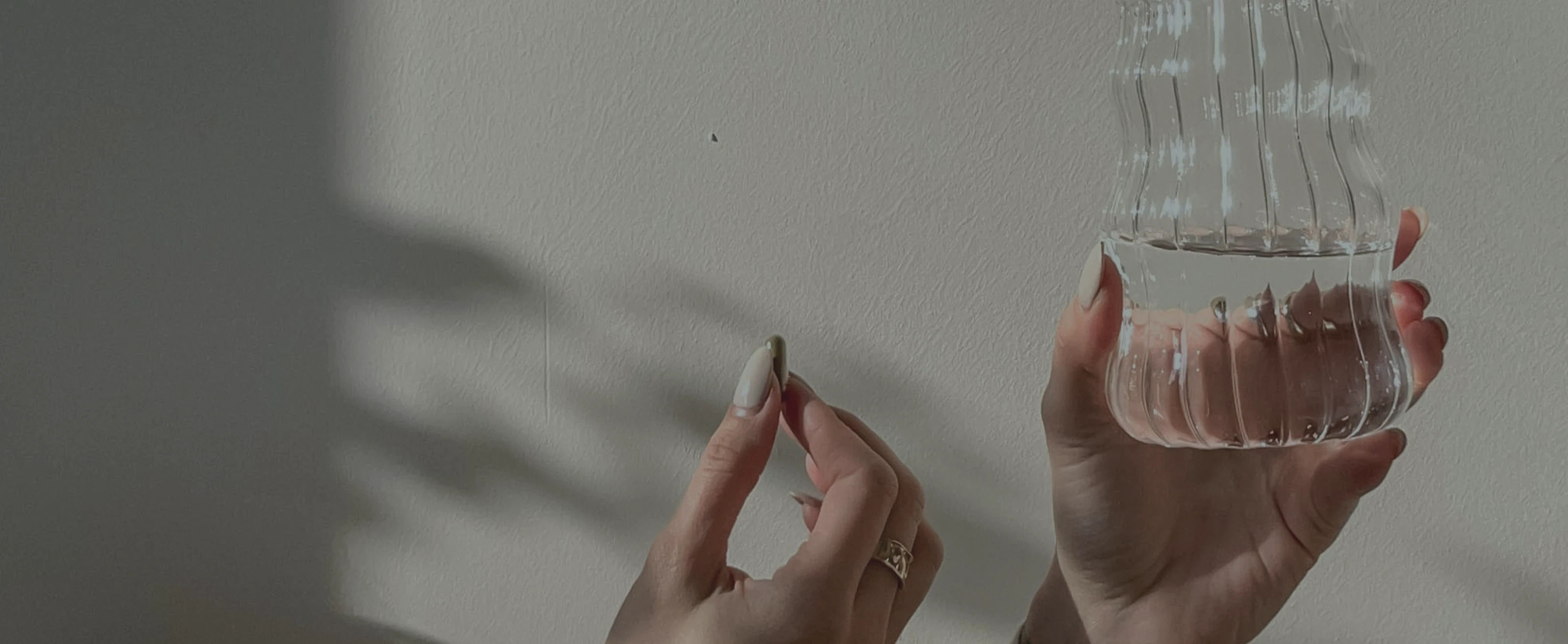 Hands holding a glass of water and a pill