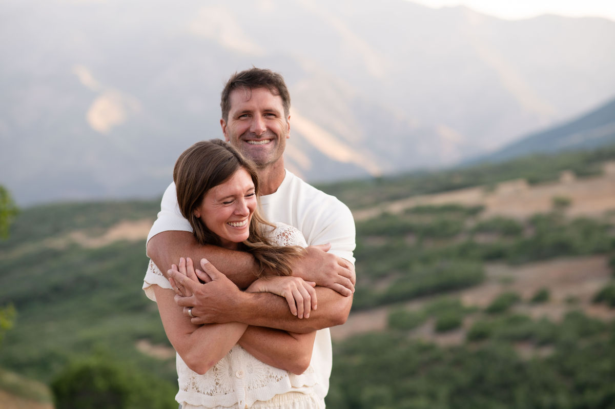 A smiling couple together outdoors against a mountain backdrop.