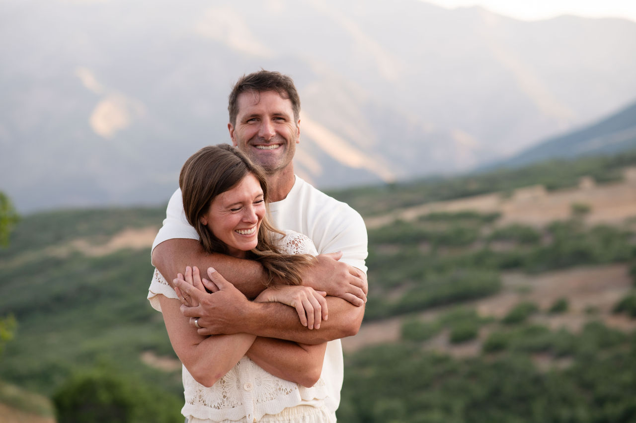 Lesli and her husband smiling together outdoors, with mountains behind them.