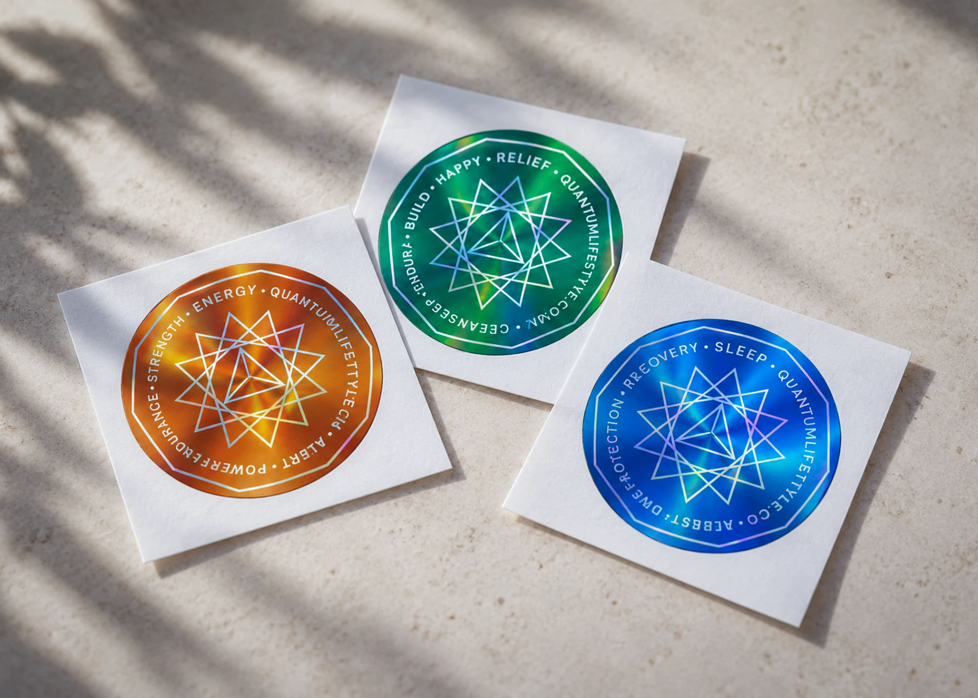 Three QuantaGrams on their backing sheets: orange, green and blue holographic stickers in soft sunlight