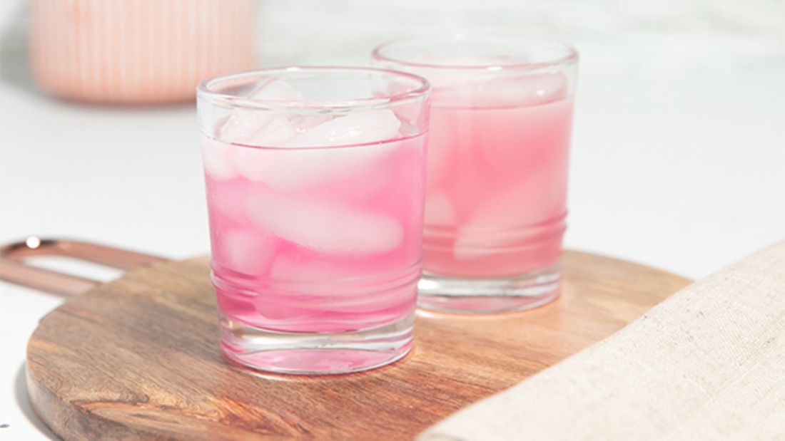 Two glasses of pink iced drinks on a wooden board.