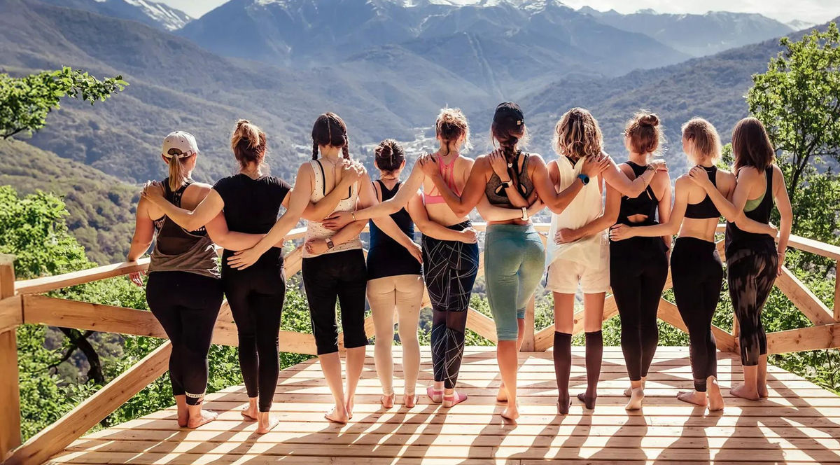 A group of women standing arm in arm on a deck overlooking the mountains