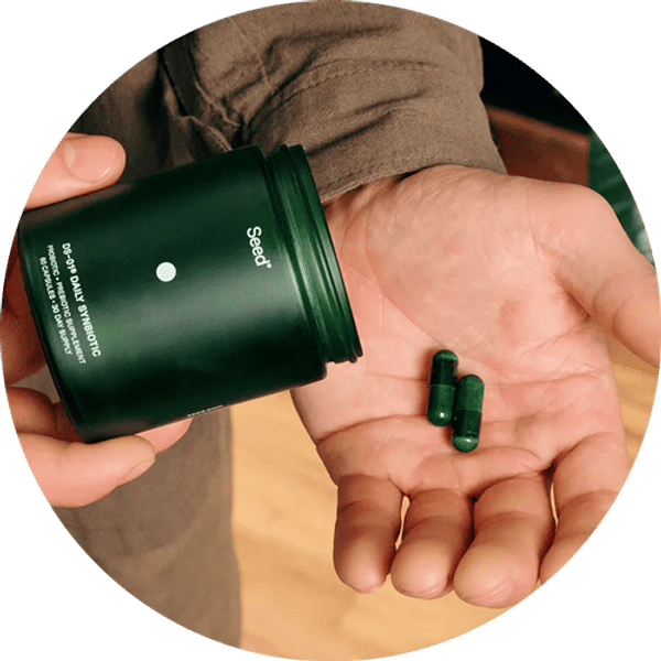 Hand holding a green container with pills spilling out, branded 'Seed'.