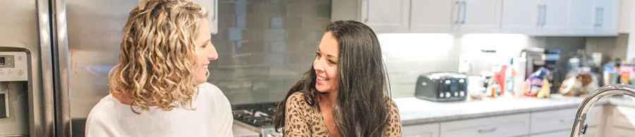 Two women chatting in a bright kitchen.