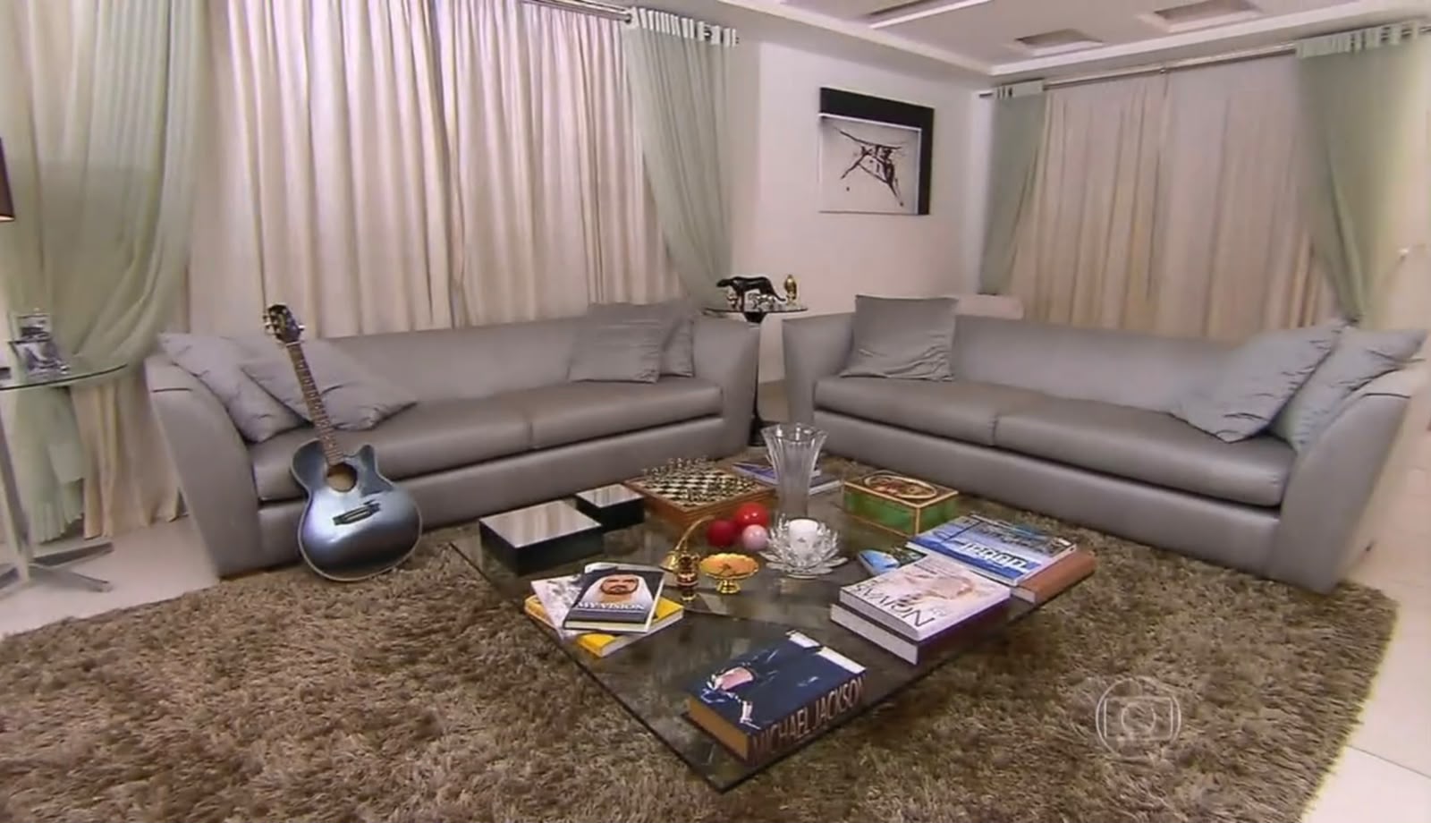 Latino conversa com Angélica na sala sofisticada de sua antiga residência, que tinha um piano e decoração em tons prateados.