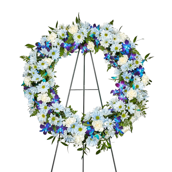 Blue Remembrance Wreath holds White Carnations, Dendrobium Orchids and Blue Daisies