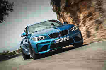 A blue BMW M2 racing around a curved road with rocky terrain in the background, exuding speed and agility.