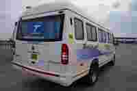 A white passenger van parked at a toll plaza, featuring "Tejas Tours & Travels" branding and clear blue curtains.