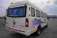 A white passenger van parked at a toll plaza, featuring "Tejas Tours & Travels" branding and clear blue curtains.