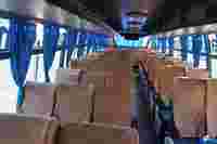 Empty bus interior with rows of upholstered seats, blue curtains along the windows, and a bright, airy atmosphere.