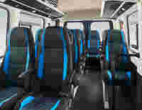 Interior of a passenger van with rows of modern, black and blue seats, spacious layout, and overhead storage.