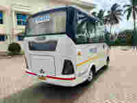 A white travel bus labeled "TEJAS" parked outside a building, surrounded by palm trees and a paved area.