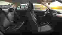 Interior view of a modern car showcasing black seats, a sleek dashboard, and a scenic waterfront backdrop with buildings.