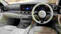 Luxurious car interior featuring a modern dashboard, touchscreen displays, and a sleek steering wheel in cream leather.