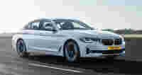 A sleek white BMW sedan drives on an asphalt road, showcasing its modern design and performance features.