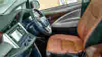 Interior of a vehicle featuring a brown leather driver's seat, steering wheel, and dashboard with controls and a display screen.