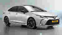 Sleek white Toyota sedan with black alloy wheels, detailed front grille, and shiny surface, set against a gray backdrop.