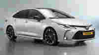 Sleek white Toyota sedan with black alloy wheels, detailed front grille, and shiny surface, set against a gray backdrop.