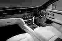 Luxurious car interior featuring white leather seats, sleek wooden accents, and high-tech dashboard controls.