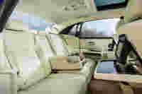 Luxurious car interior with creamy leather seats, a wooden armrest console, and dual screens, set in a bright atmosphere.