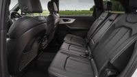 Spacious, modern car interior showing five black leather seats, with a view of greenery through the windows.