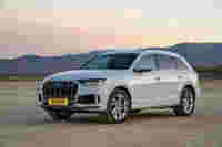 Silver Audi Q7 SUV parked in a desert landscape with mountains and a pastel sunset in the background.