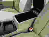 Car interior featuring beige upholstery, a console with an open storage compartment, and cup holder beside it.