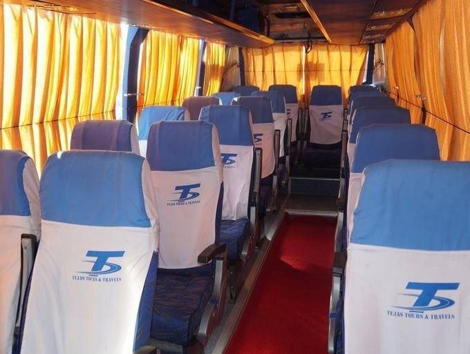 Empty bus interior with blue and white seats, red carpet aisle, and yellow curtains, suggesting a travel setup.