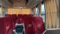 Inside a tour bus with maroon seats and yellow curtains, ready for passengers. The mood is calm and waiting.