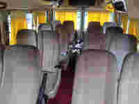 Interior of a van featuring rows of patterned seats and yellow curtains, creating a spacious and inviting atmosphere.